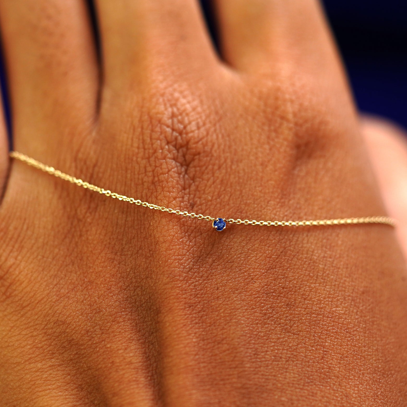A solid gold sapphire Gemstone Cable Necklace resting on the back of a model's hand