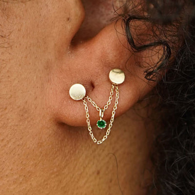 Close up view of a model's ear wearing a yellow gold emerald Cable Chain Connector across two Circle Studs on their lobe