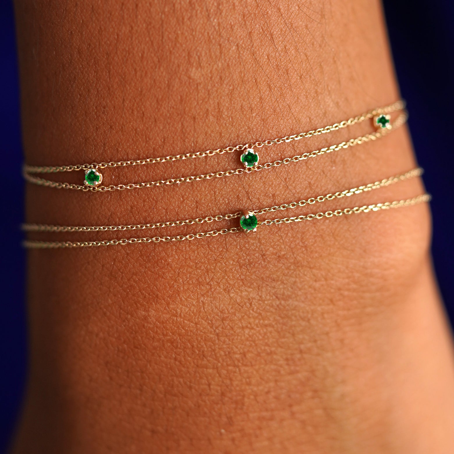 A model's wrist wearing the emerald versions of both a 3 gemstone cable bracelet and a gemstone cable bracelet layered 