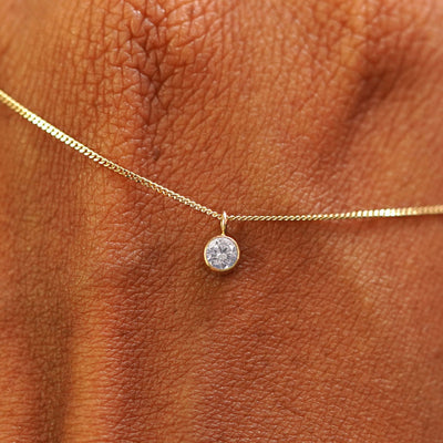 Close up view of a 14k yellow gold Moissanite Necklace draped across the back of a model's hand