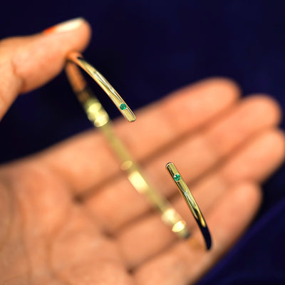 A yellow gold emerald Gemstone Open Bangle Bracelet resting between a model's fingers