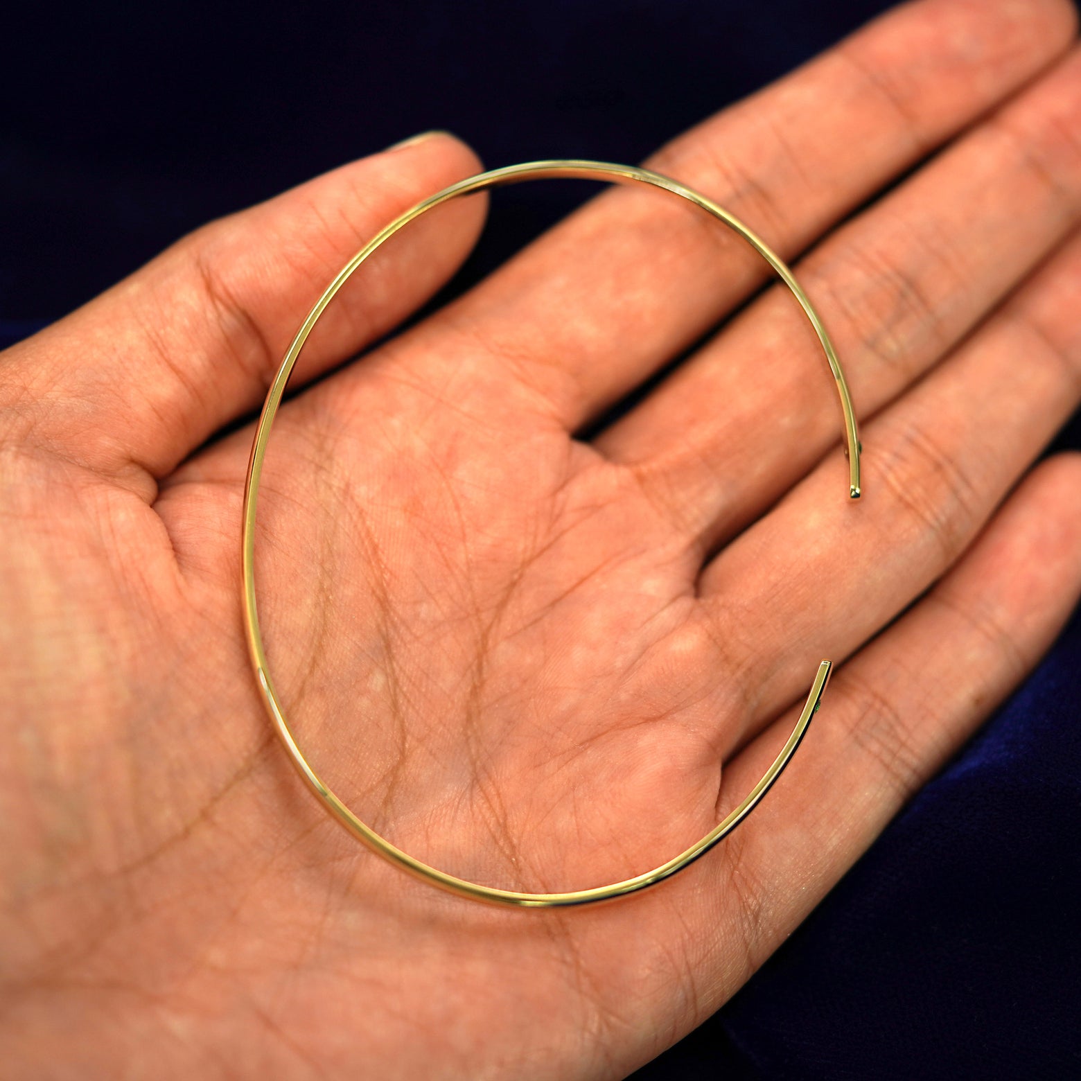 A yellow gold emerald Gemstone Open Bangle Bracelet sitting in a model's palm