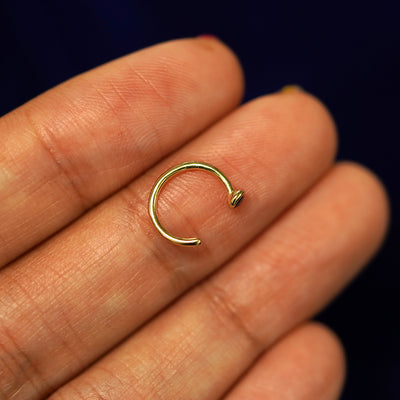 A 14k yellow gold sapphire gemstone Open Hoop resting flat on a models fingertips to show the thickness of the earring