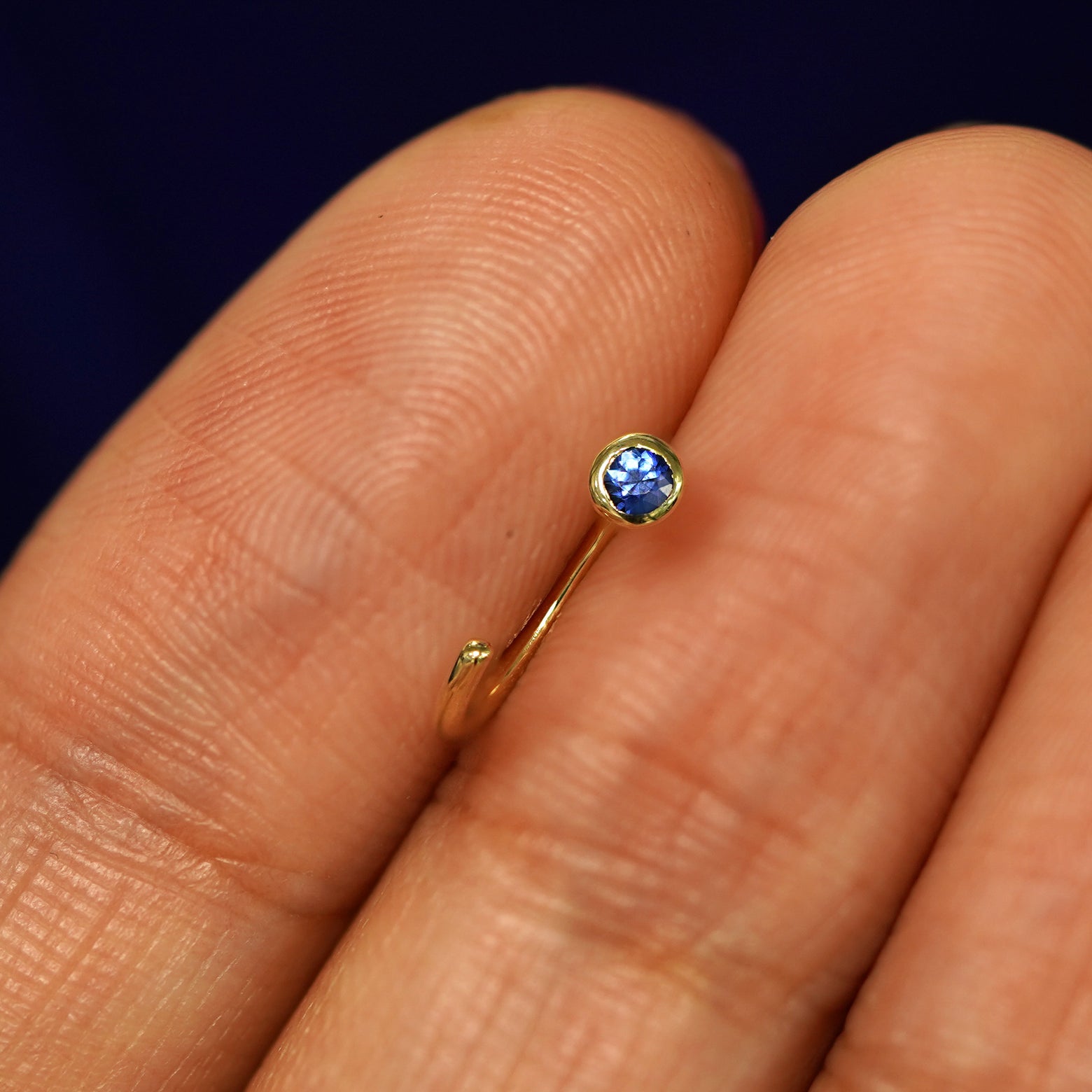 A Sapphire Open Hoop between a models fingers to show the detail of the bezel set stone
