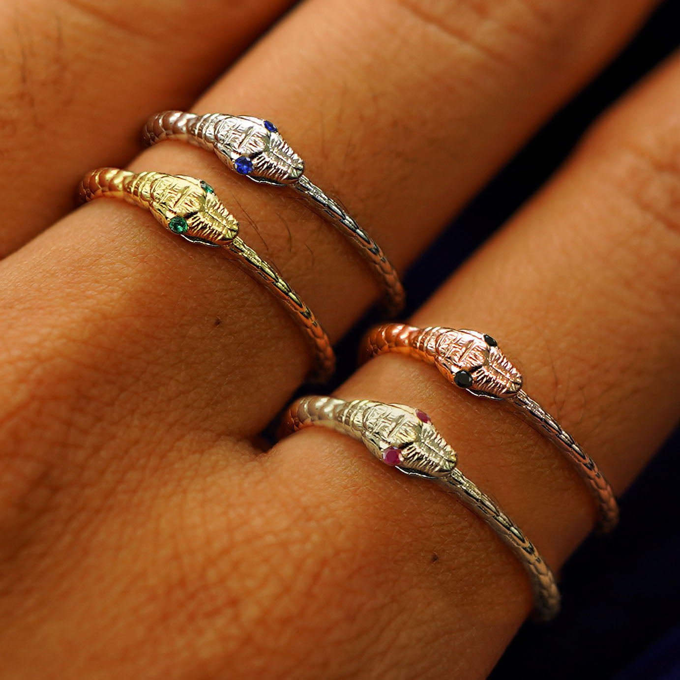 A model's hand wearing four versions of the Gemstone Ouroboros ring in variations of yellow, white, rose, and champagne gold
