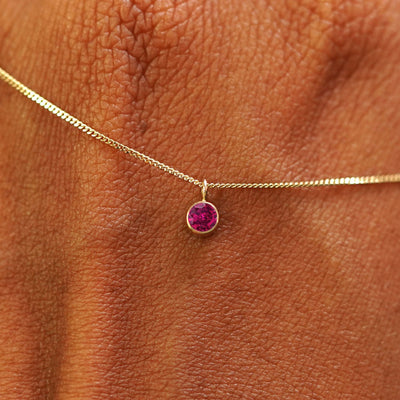 Close up view of a 14k yellow gold Ruby Necklace draped across the back of a model's hand