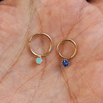 A 10mm opal pierced septum and an 8mm sapphire pierced septum resting in a model's palm