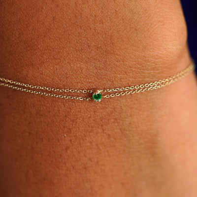 Close up view of a model's wrist wearing a solid gold Gemstone Cable Bracelet in emerald