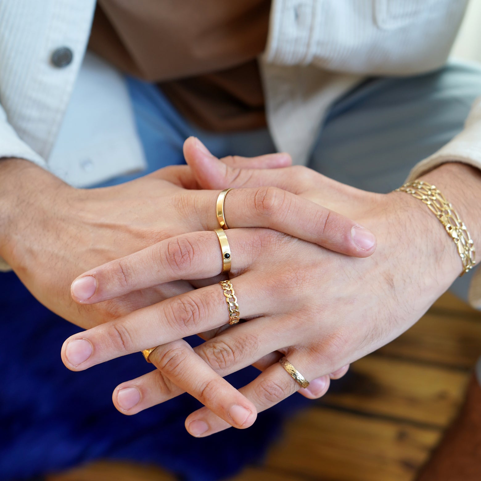 A model sitting with their fingers clasped and their arms resting on their knees wearing various Automic Gold rings