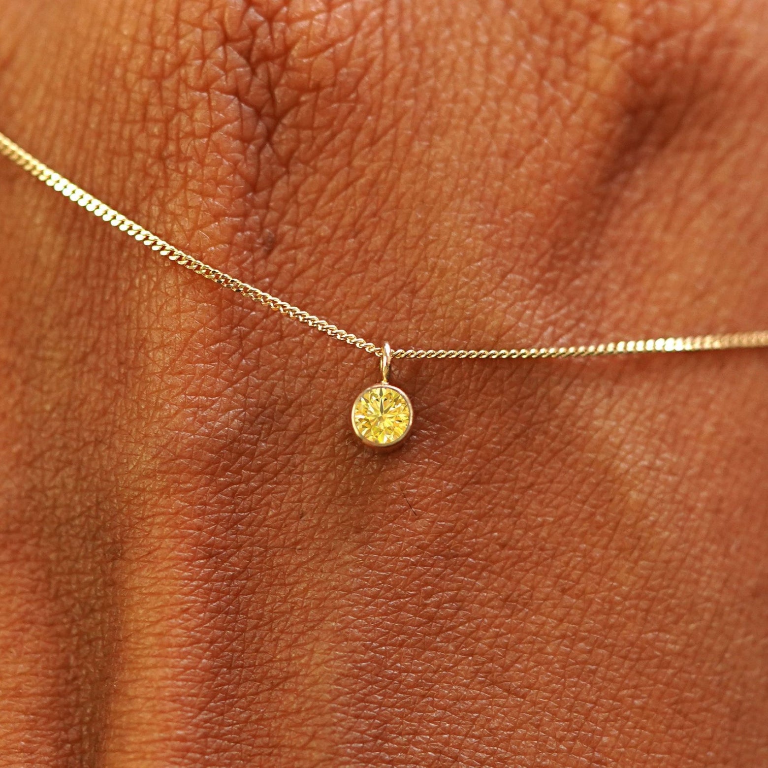 Close up view of a 14k yellow gold Yellow Diamond Necklace draped across the back of a model's hand