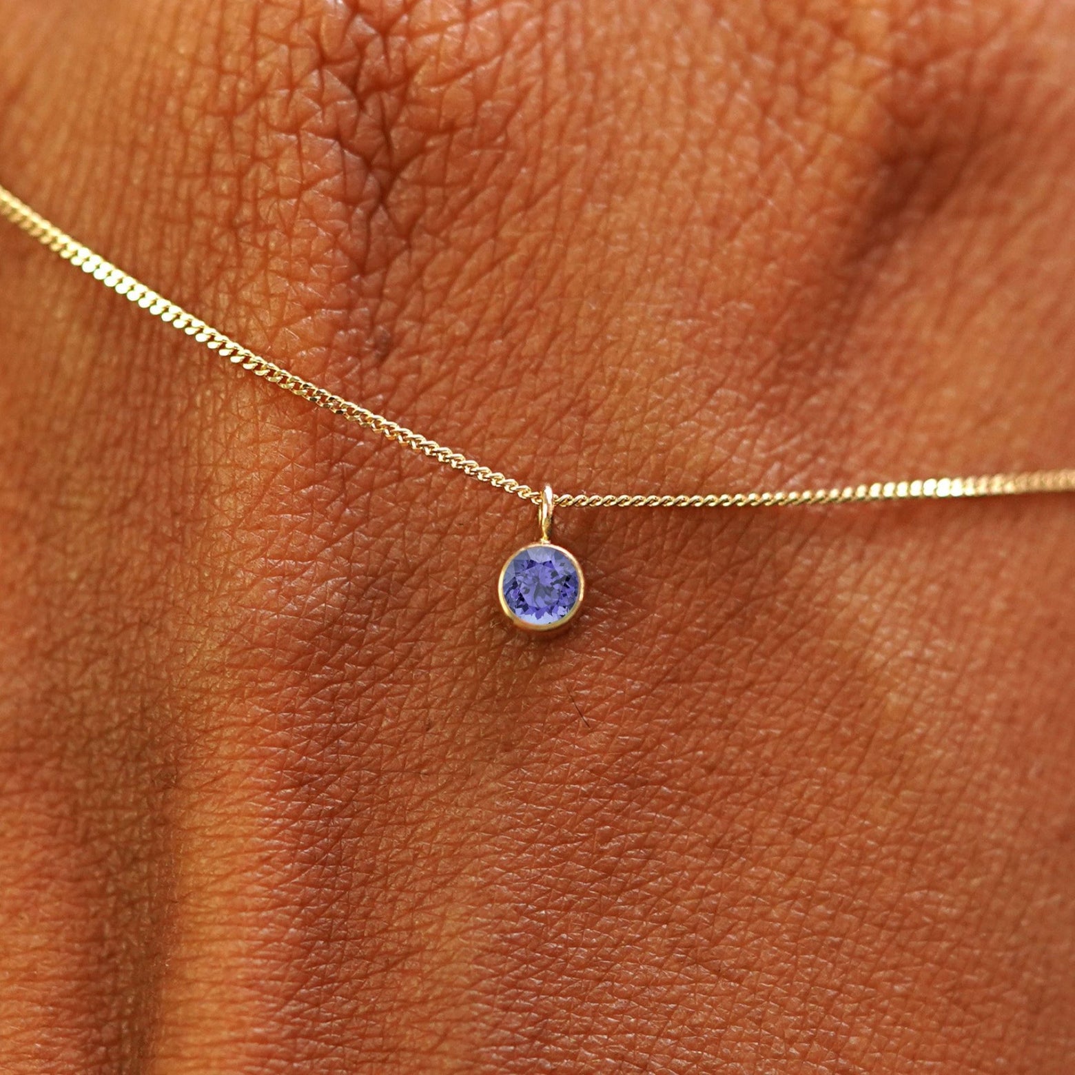 Close up view of a 14k yellow gold Tanzanite Necklace draped across the back of a model's hand