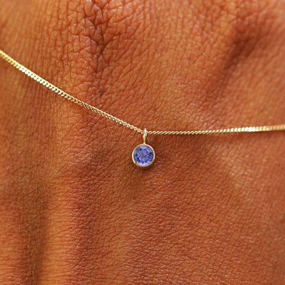 Close up view of a 14k yellow gold Tanzanite Necklace draped across the back of a model's hand