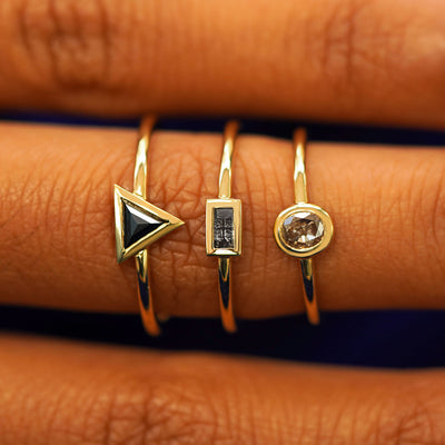 An Oval Champagne Diamond, a Baguette Salt and Pepper Diamond, and a Trillion Black Diamond Ring stacked on a model's finger