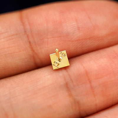 A yellow gold Pyramid stud laying facedown on a model's fingers to show the underside view