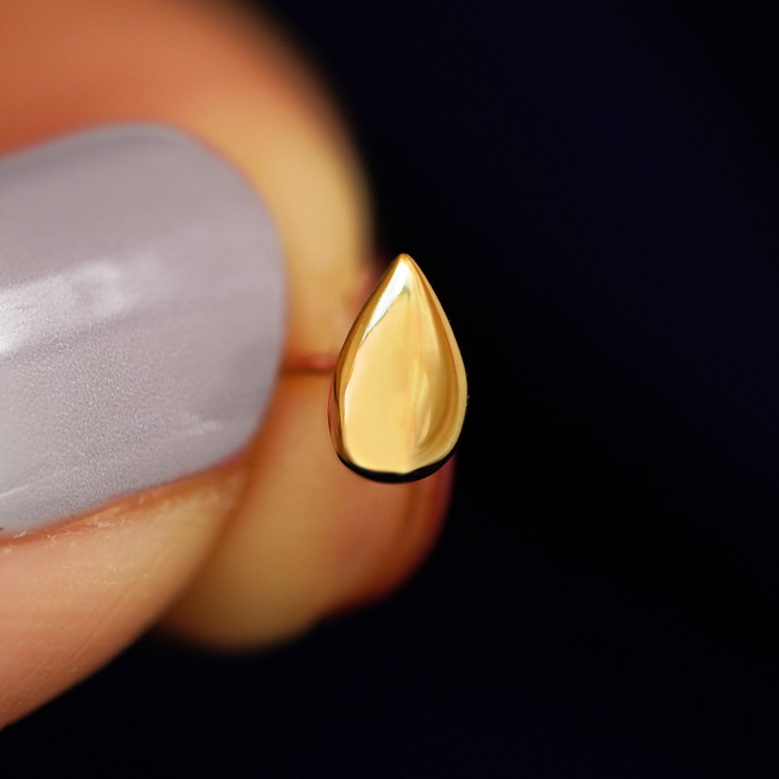 A model holding a Teardrop stud in between their finger tips to show the thickness of the Teardrop shape