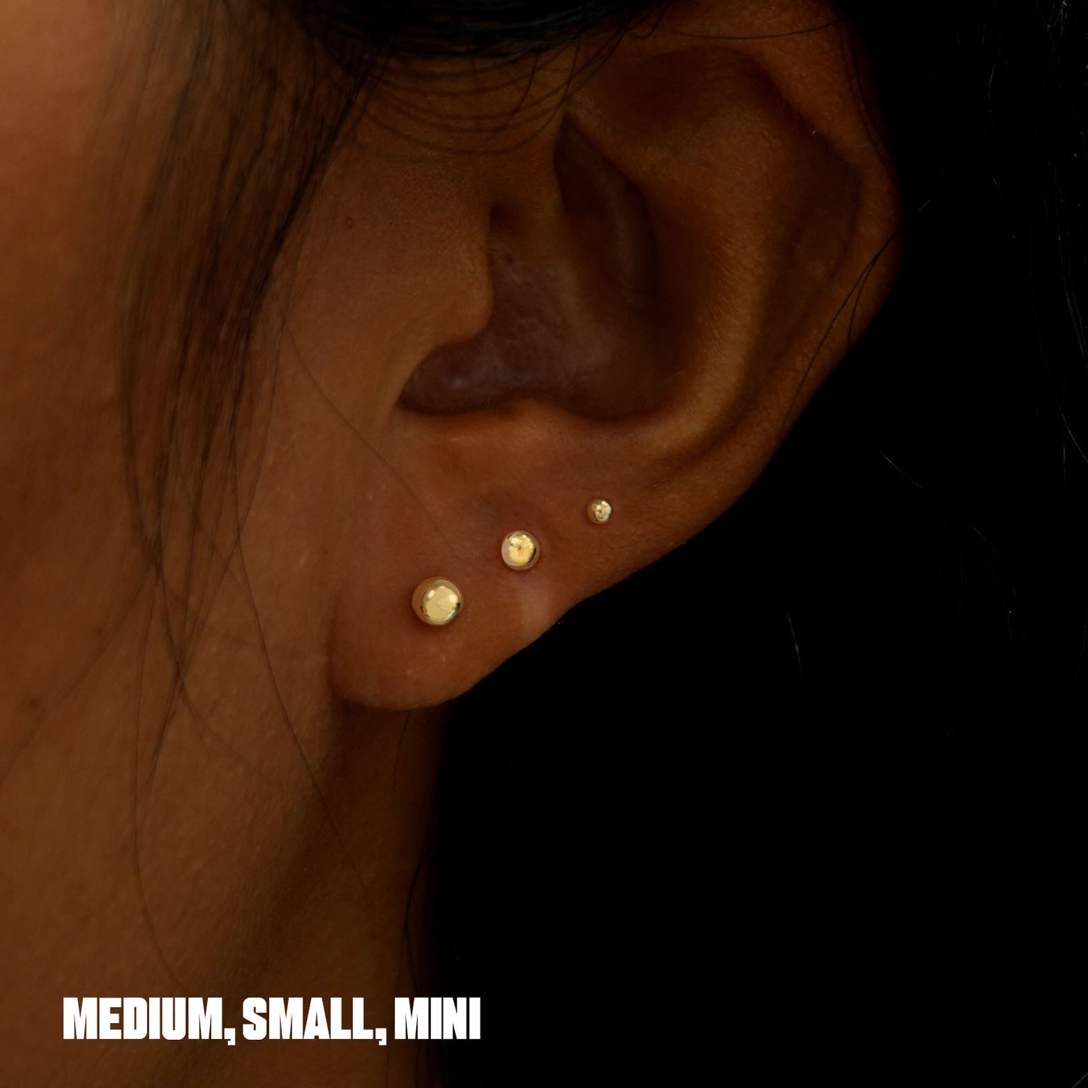 A model wearing Medium, Small, and  Mini Ball Earrings in multiple lobe piercings