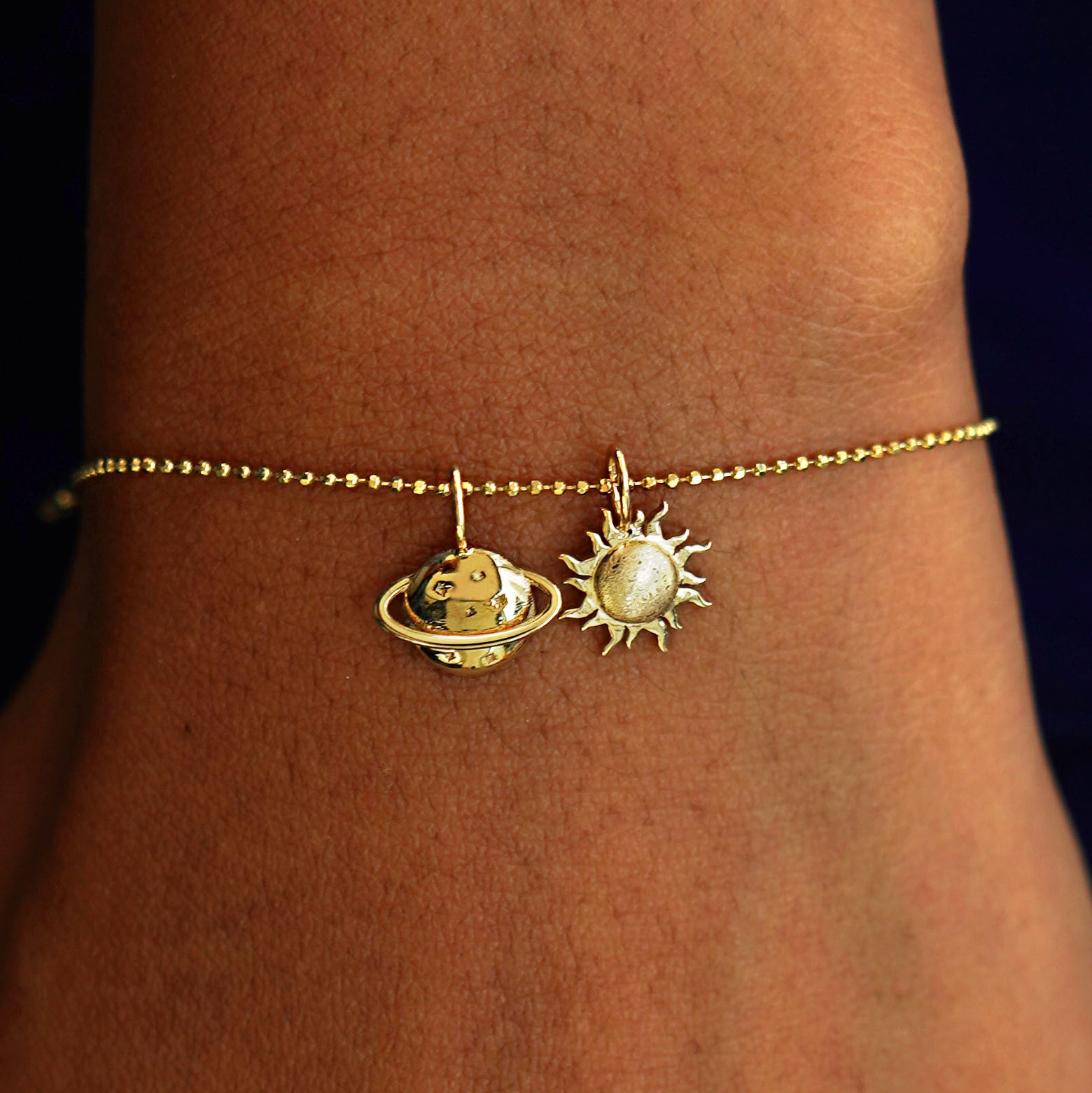 A model's wrist wearing a yellow gold Bead Chain with a Saturn Charm, and a Sun Charm