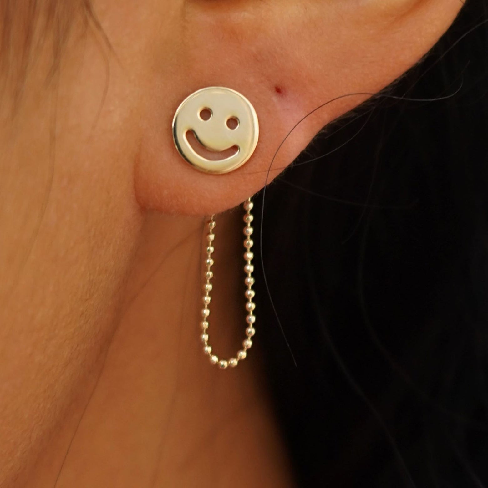 Close up view of a model's ear wearing a yellow gold Connector with both attached behind a Smiley Face Earrings