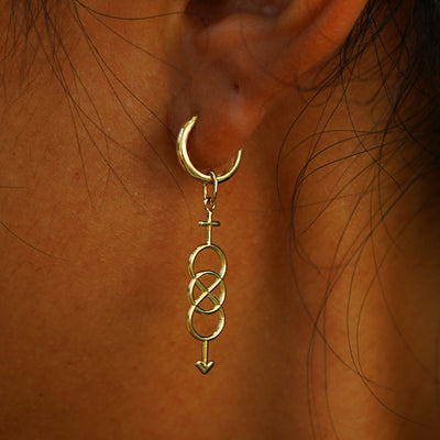 Close up view of a model's ear wearing a yellow gold Bisexual Symbol Charm on a Curvy Huggie Hoop