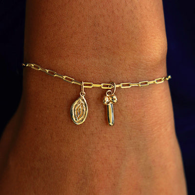 A model's wrist wearing a yellow gold Butch Chain with a Vulva Charm and a Penis Charm