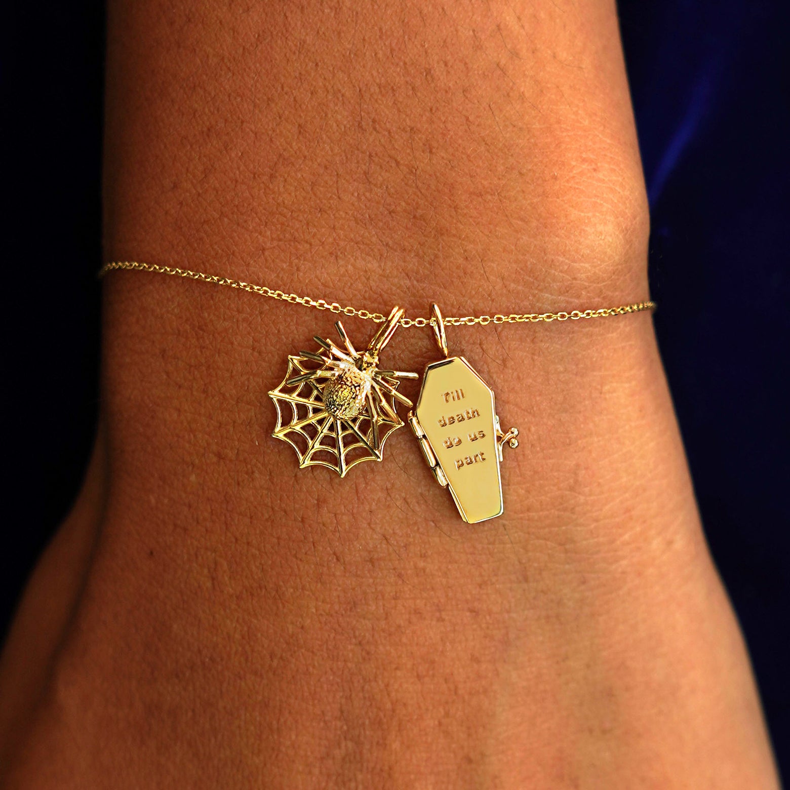 A model's wrist wearing a yellow gold Cable Chain with a Spider Web Charm and a Coffin Charm