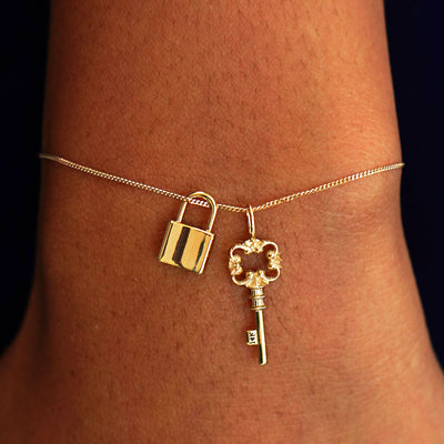 A model's wrist wearing a yellow gold Essential Chain with a Lock Charm and a Key Charm