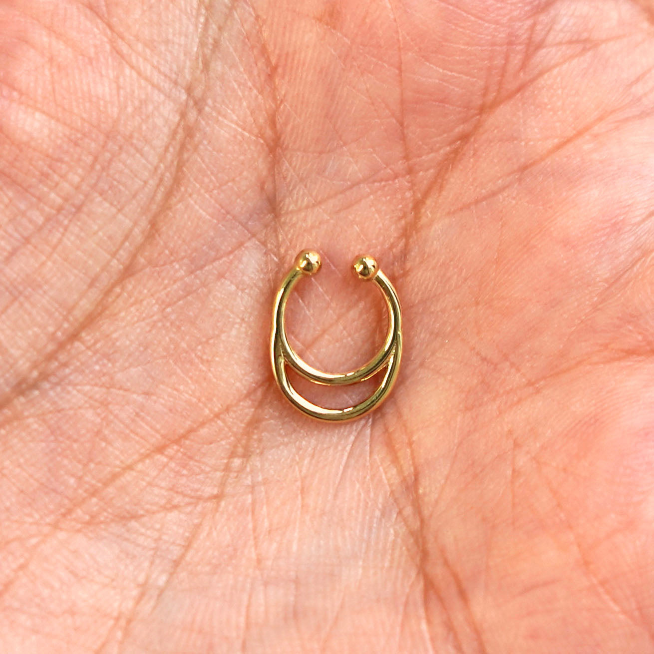 A model's hand holding a 14 karat yellow gold Non-Pierced Double Circle Septum