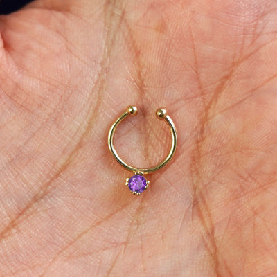 A model's hand holding a 14 karat yellow gold Non-Pierced Amethyst Gemstone Septum