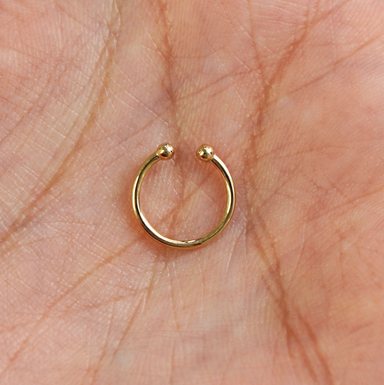 A model's hand holding a 14 karat yellow gold Non-Pierced Line Septum