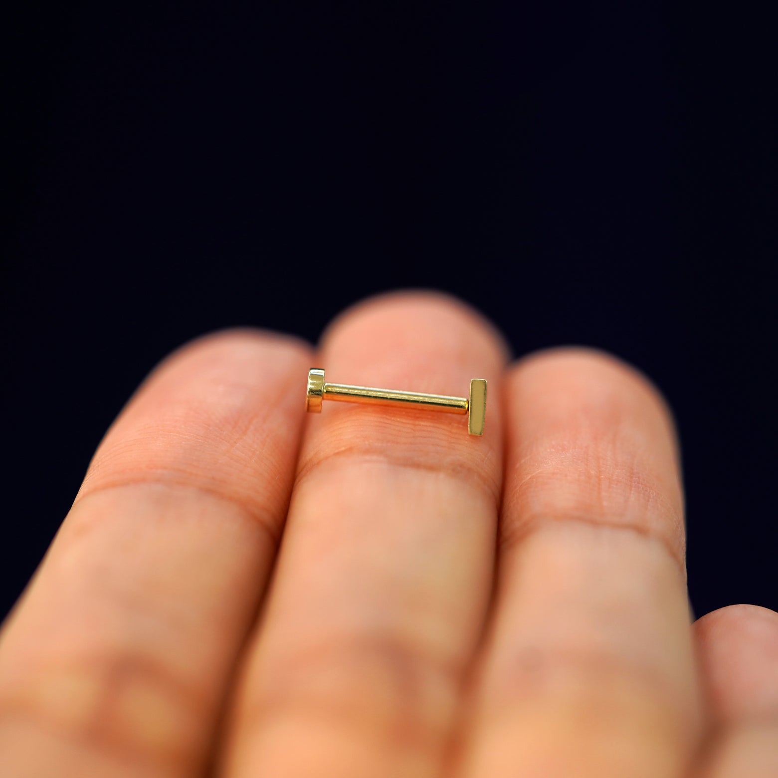 Side view of a yellow gold Triangle Flatback Piercing on a model's fingertips