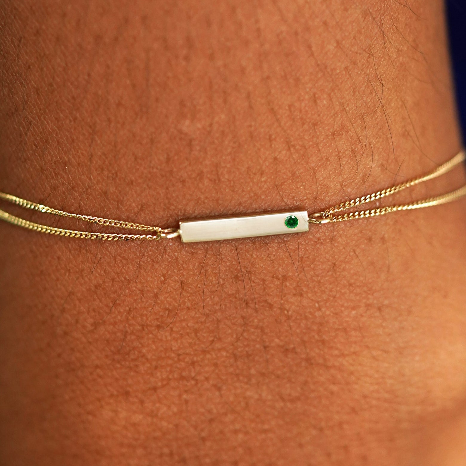 Close up view of a model's wrist wearing a solid yellow gold emerald Gemstone Bar Bracelet