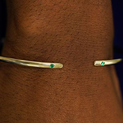 Close up view of a model's wrist wearing a yellow gold emerald Open Bangle