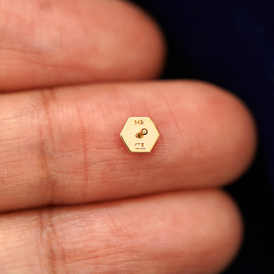 A yellow gold Hexagon stud laying facedown on a model's fingers to show the underside view