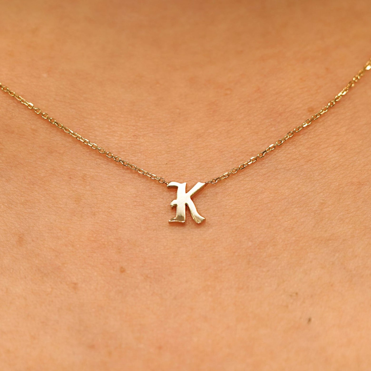 Close up view of a model's neck wearing a 14k solid yellow gold Initial Necklace in the letter K