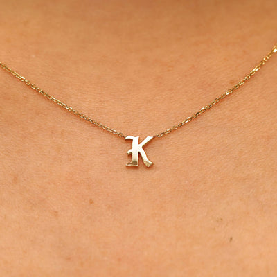 Close up view of a model's neck wearing a 14k solid yellow gold Initial Necklace in the letter K