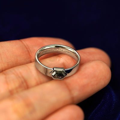 A white gold Hexagon Diamond Band in a model's hand engraved with the words Written In The Stars