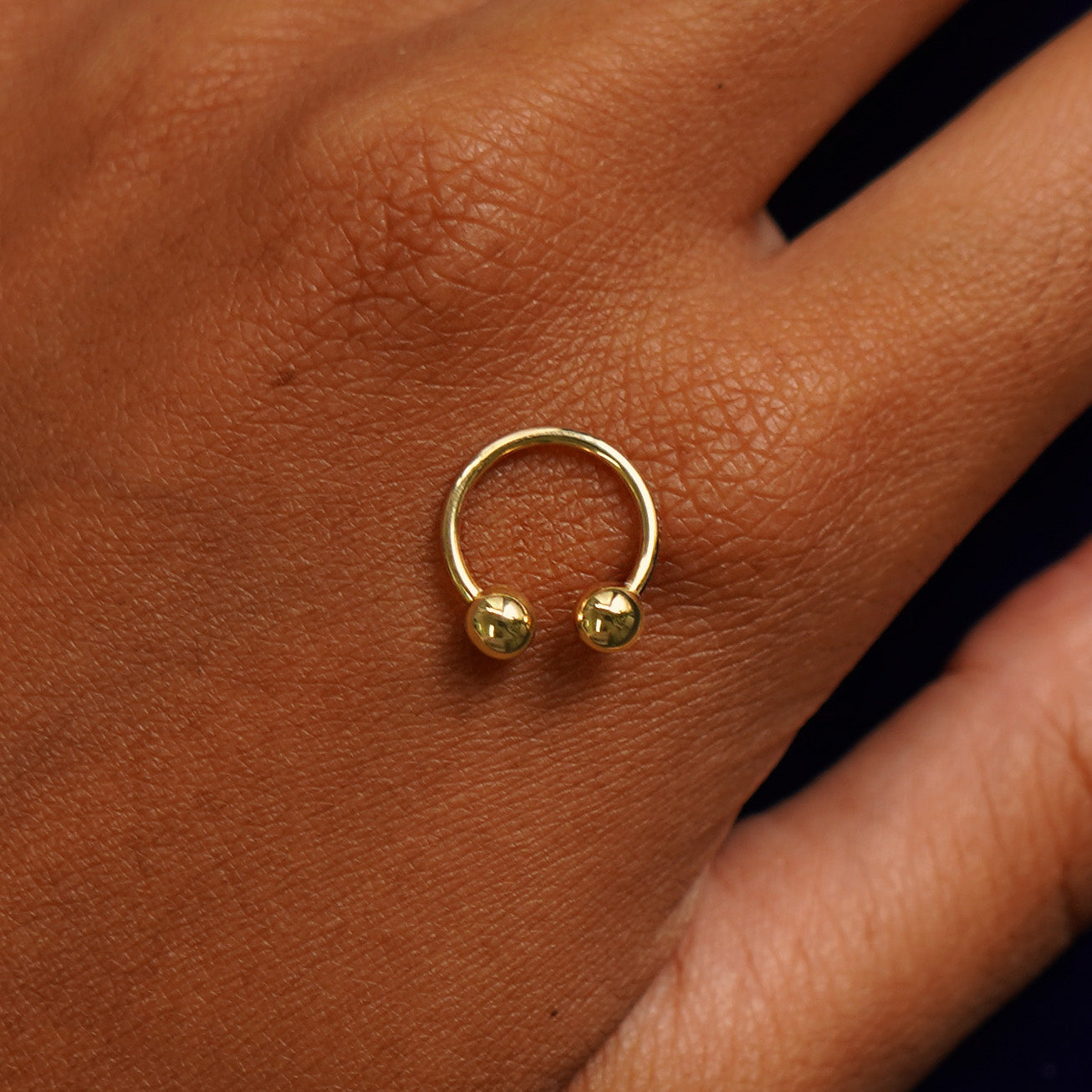 A yellow gold small horseshoe piercing resting on the back of a model's hand to indicate size