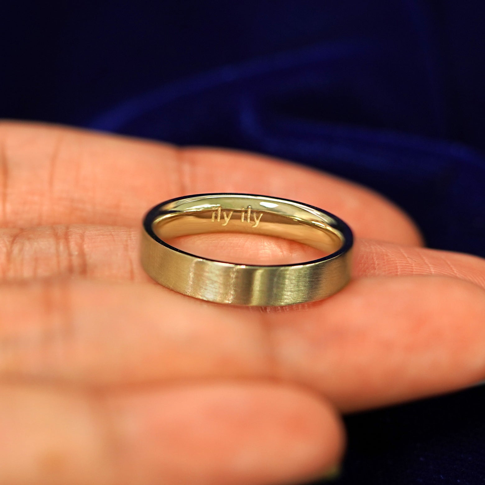 A yellow gold Industrial Matte Band in a model's hand engraved with the words ily ily