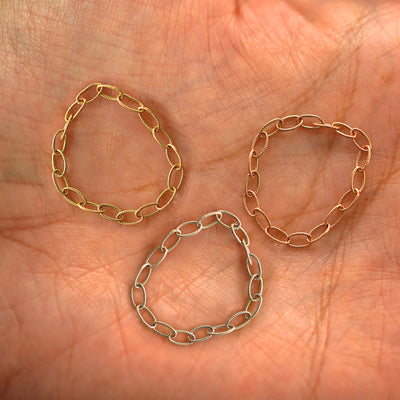 Three versions of the Veren Chain Ring shown in options of yellow, white and rose gold sitting in a model's palm