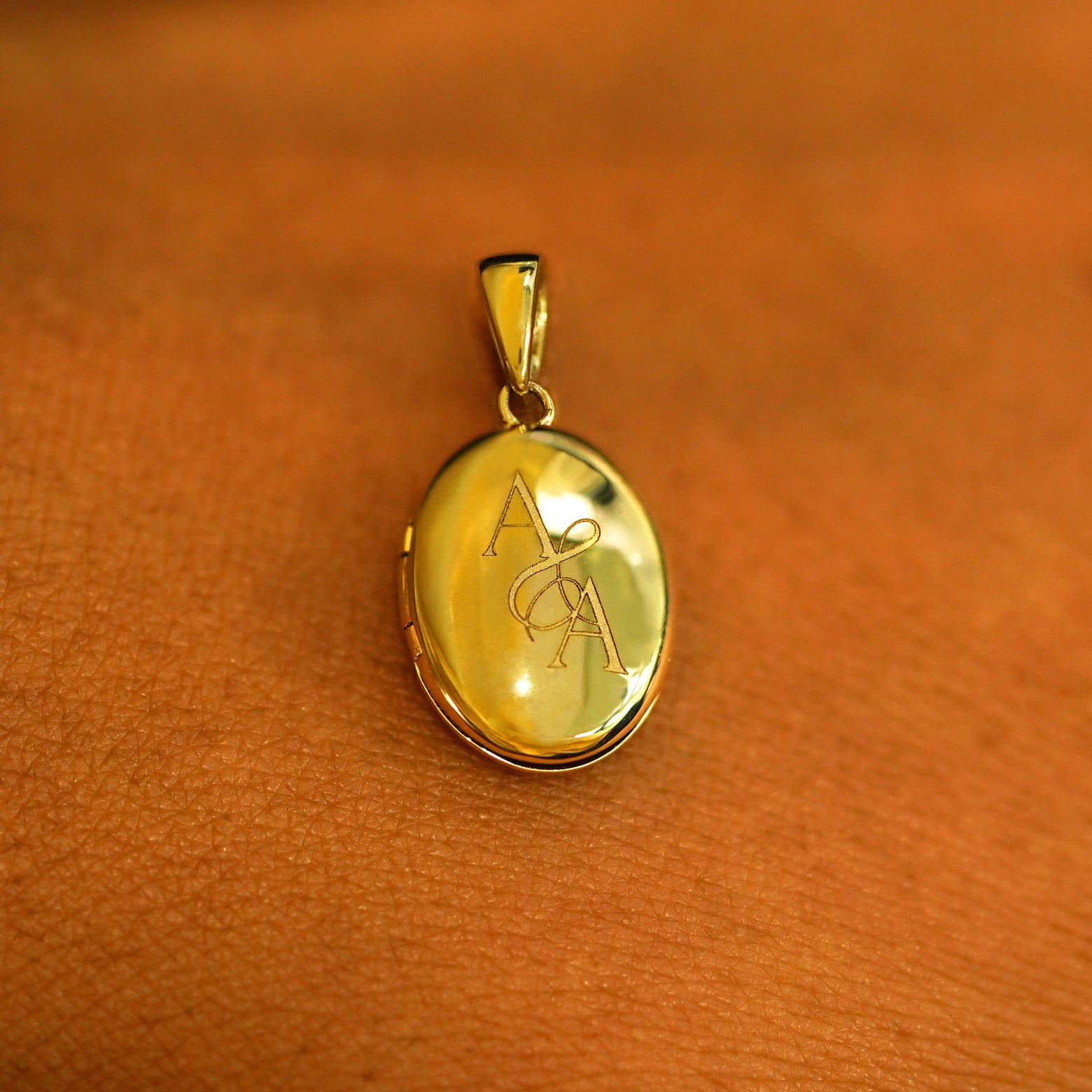 A 14k yellow gold Oval Locket Pendant on the back of a model's hand showing the engraving A & A on the back