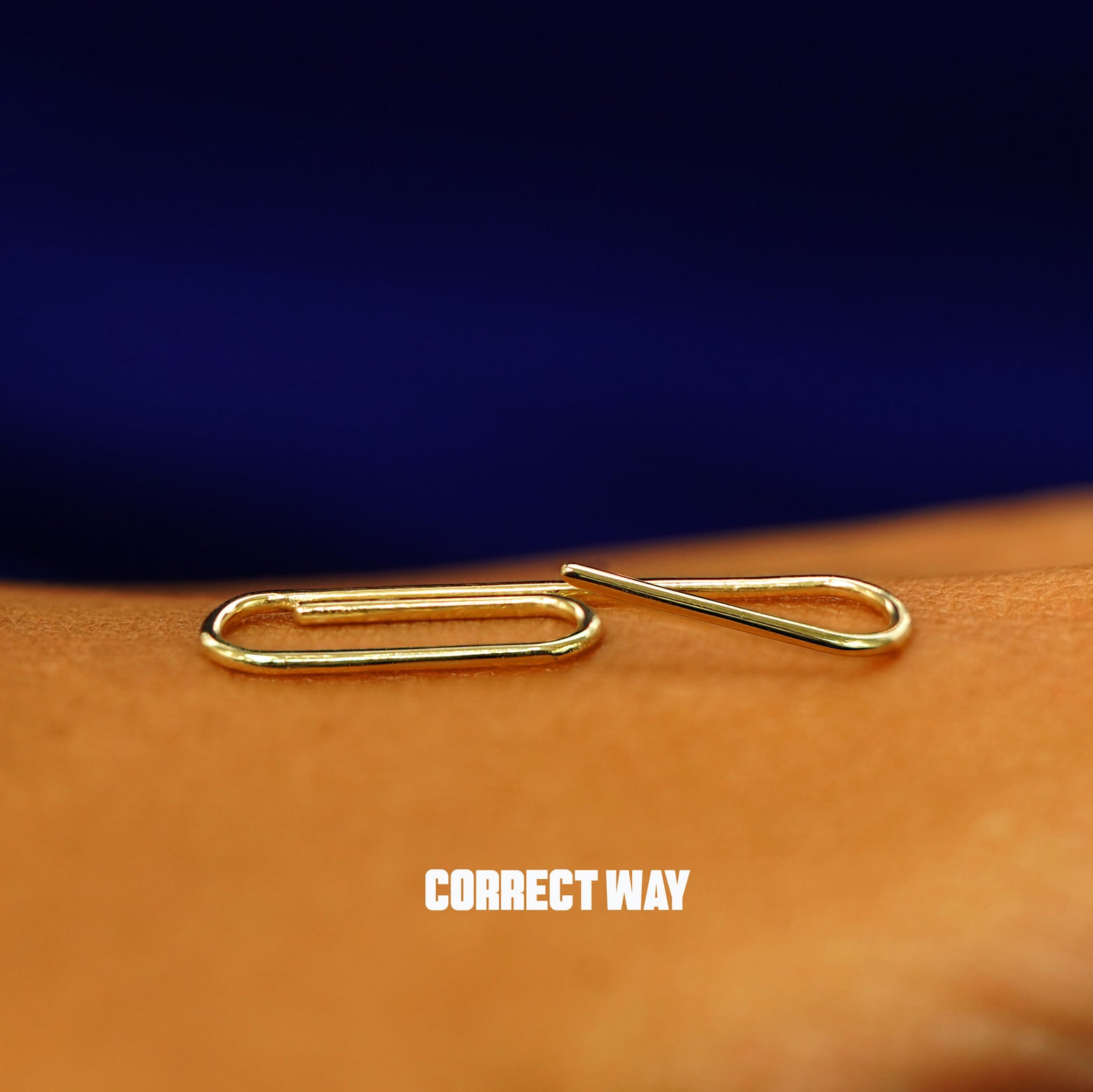 A yellow gold Not A Paperclip Earring on the back of a model's hand showing the correct way to open the earring