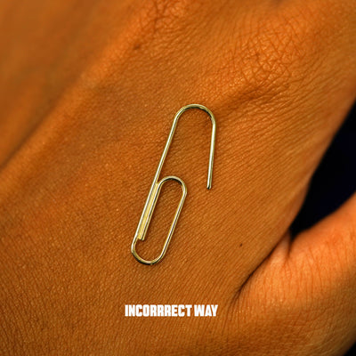 A yellow gold Not A Paperclip Earring on the back of a model's hand showing the incorrect way to open the earring