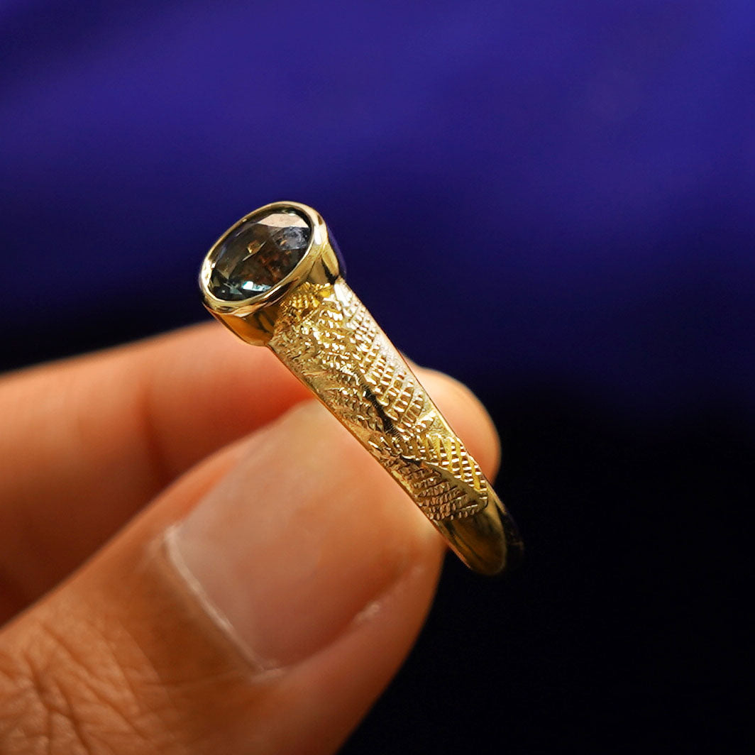 A model holding a Dark Green Sapphire Pine Ring tilted to show the details of the ring