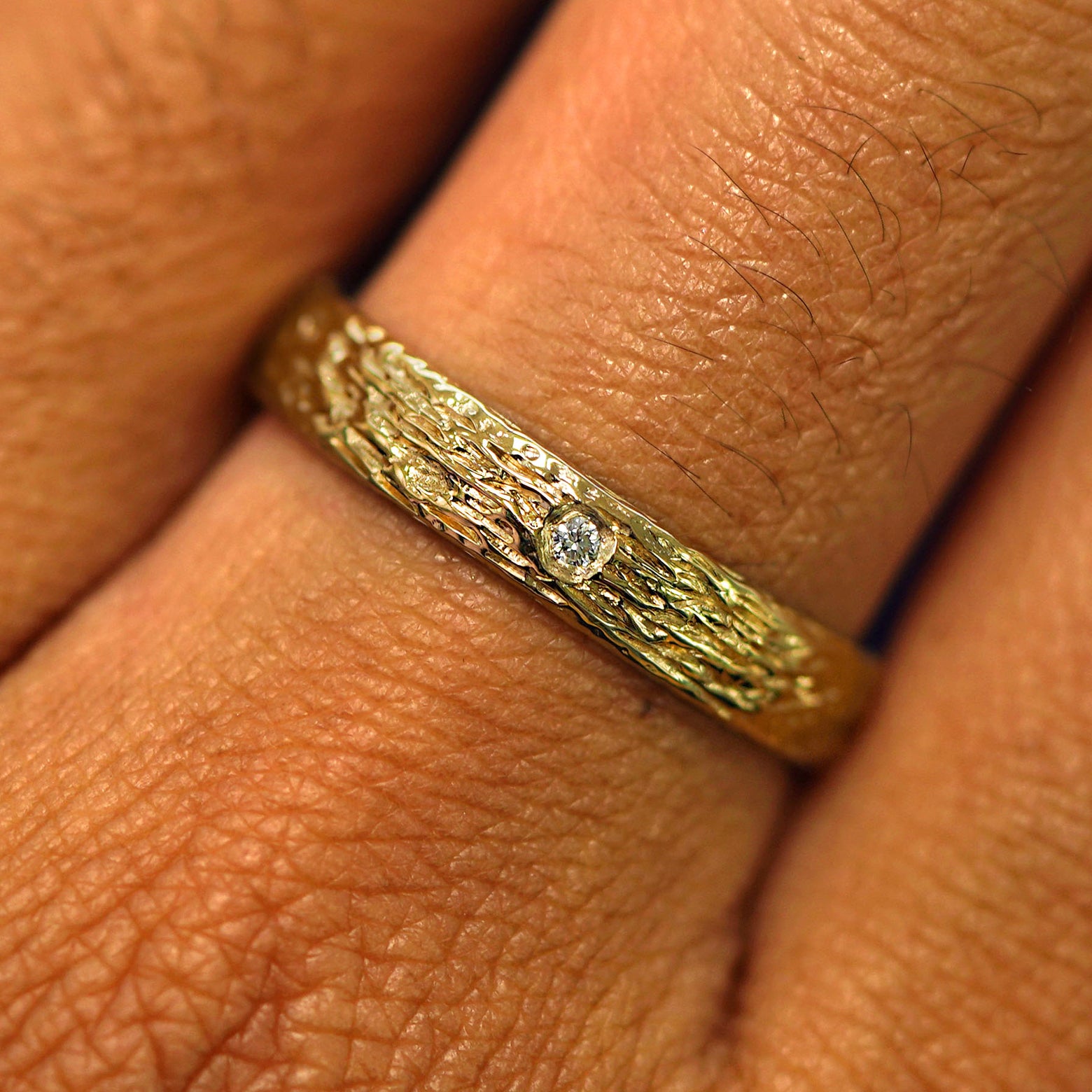 Close up view of a model's hand wearing a solid yellow gold Raw Band with one diamond