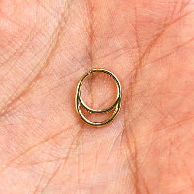 A model's hand holding a 14 karat yellow gold Pierced Double Circle Septum