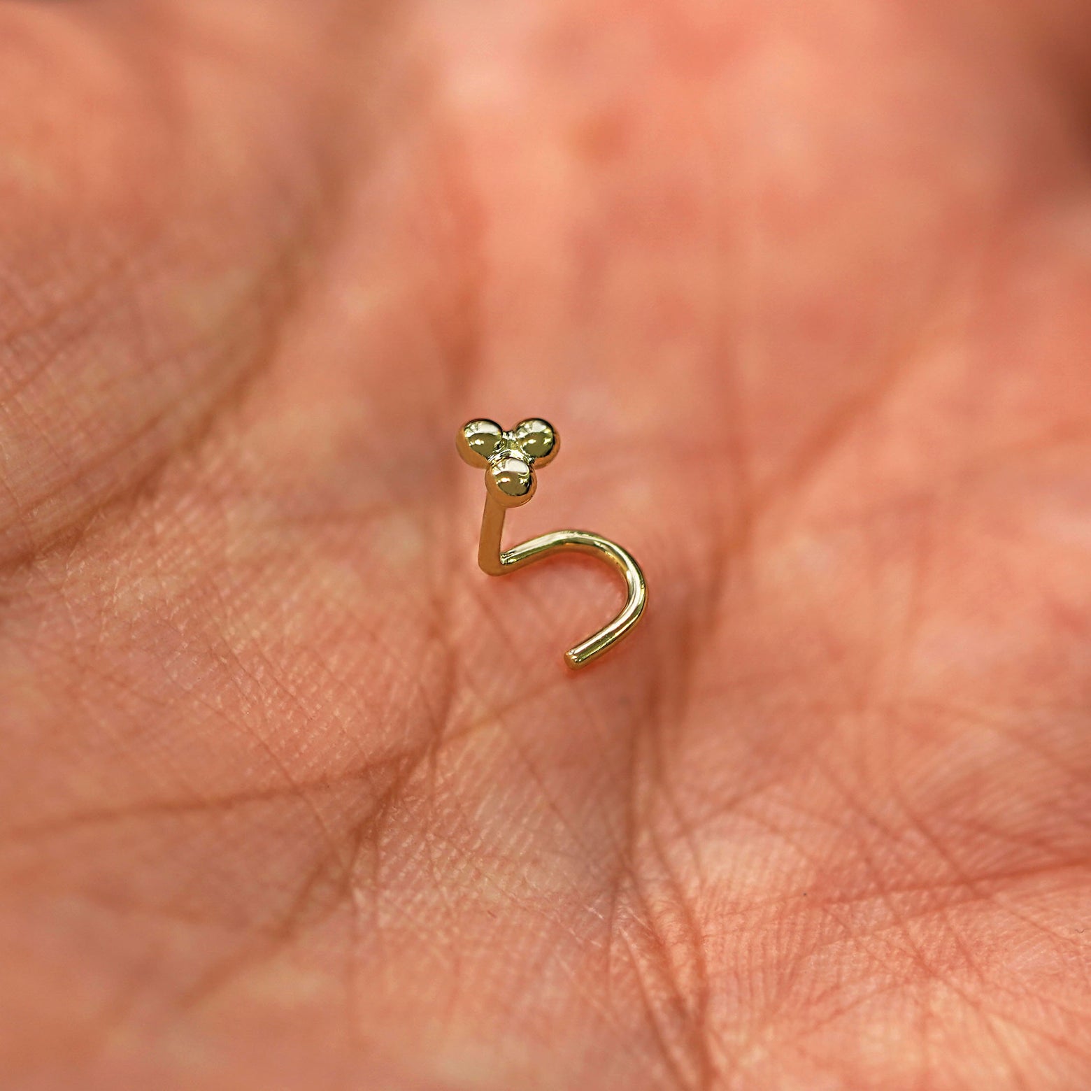 A 14 karat yellow gold Ball Trio Nose Stud standing upright to show detail and resting in the palm of a model's hand