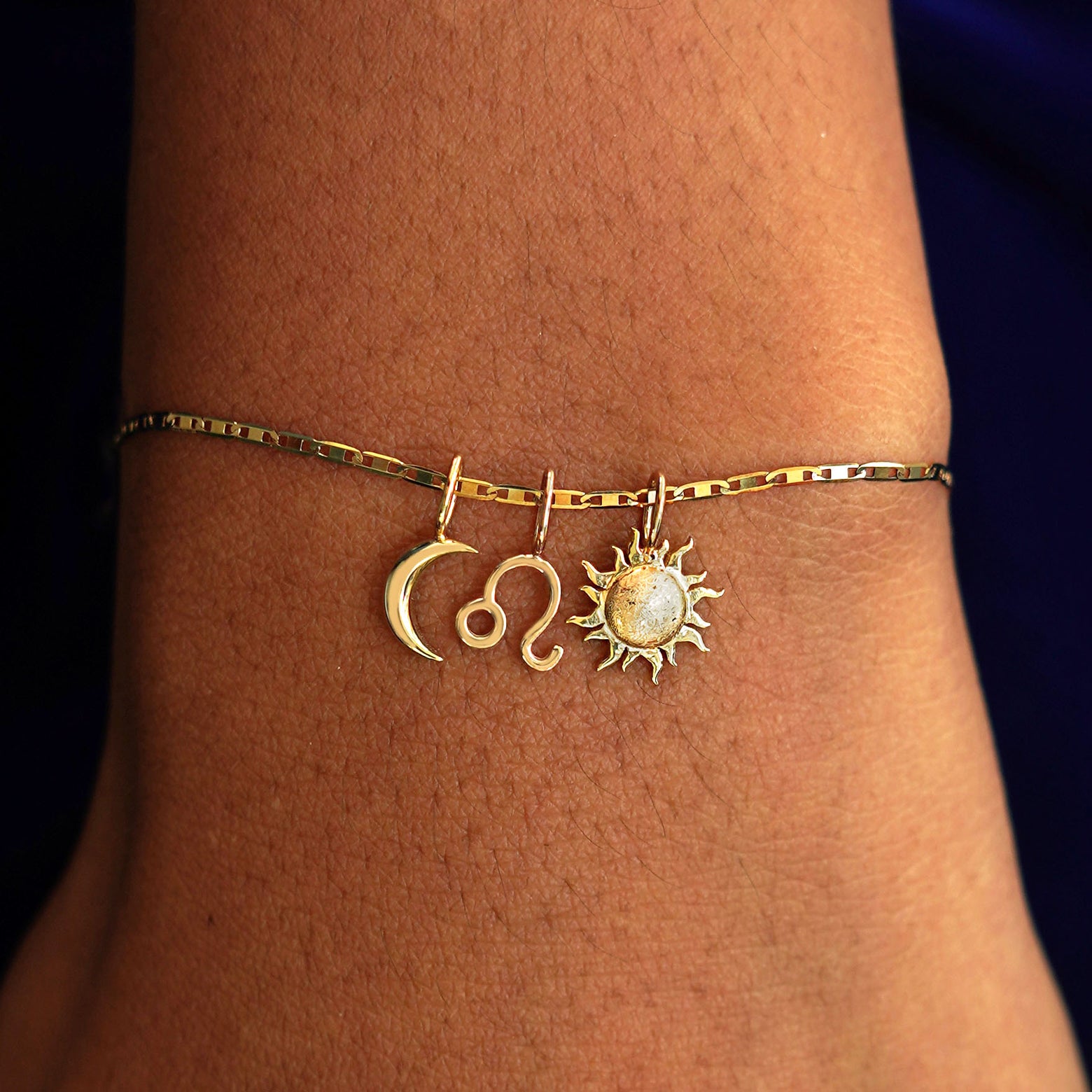 A model's wrist wearing a yellow gold Valentine Chain with a Moon Charm, A Zodiac Charm, and a Sun Charm