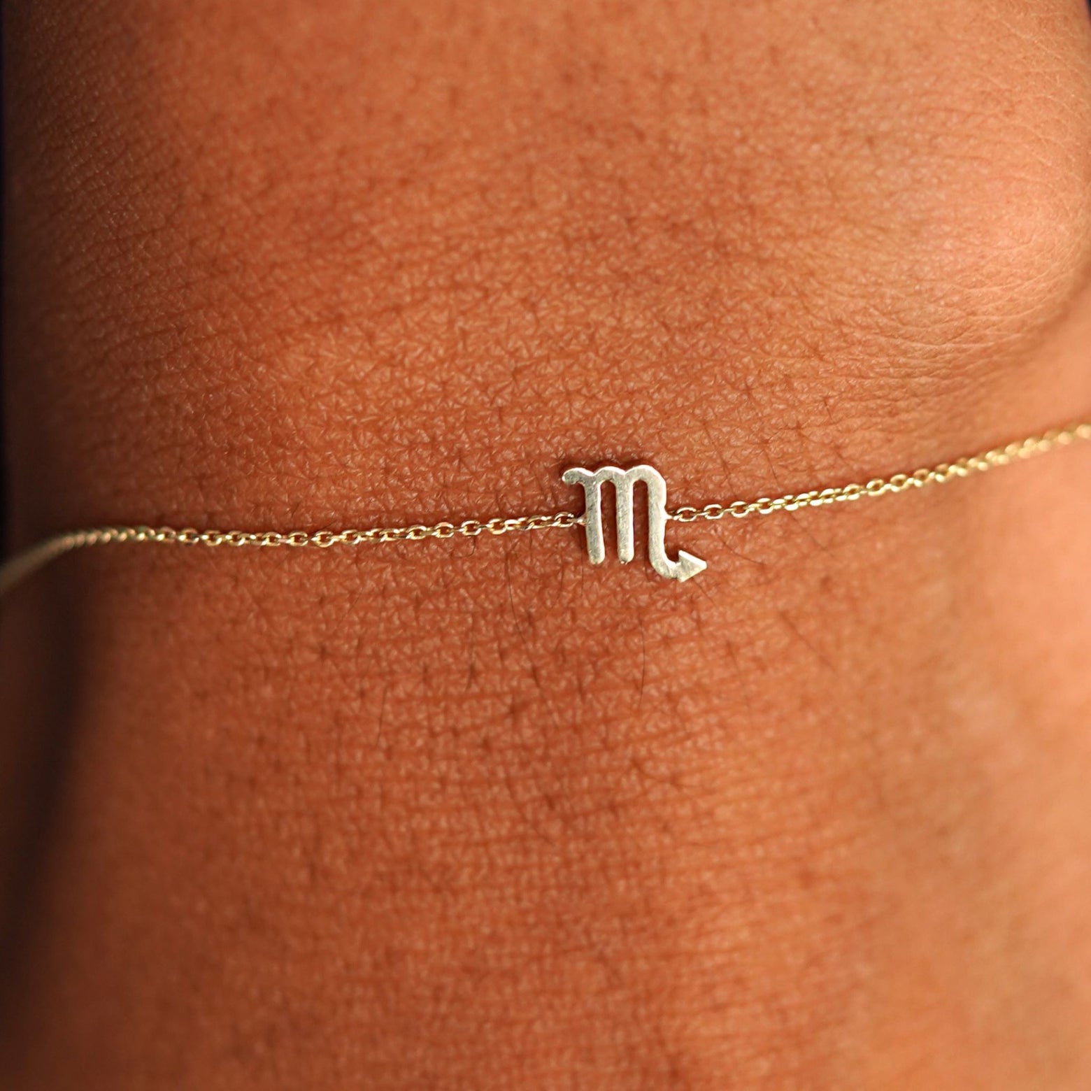 Close up view of a model's wrist wearing a solid yellow gold Scorpio Horoscope Bracelet