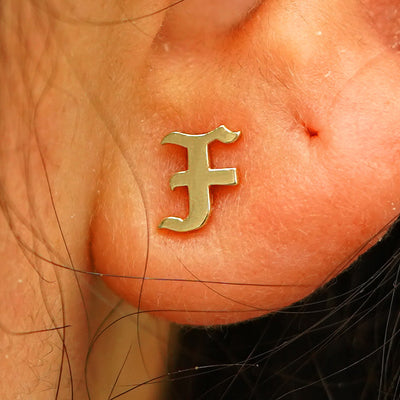 Close up view of a model's ear wearing a yellow gold Initial Earring in the letter F