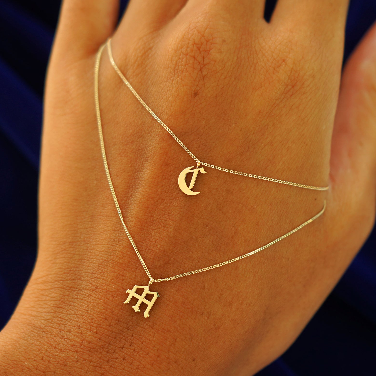 Twonitial Charm Necklaces with the letters C and M draped across the back of a model's hand